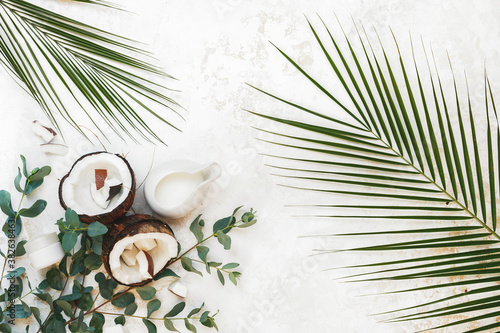 Natural and organic spa still life ingredients with fresh coconut, moisturizer cream and collection of different green leaves on rustic white surface. Top view, blank space