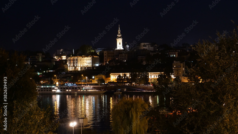 Belgrade Serbia Downtown Night Cityscape Timelapse with Light Reflections on the Sava River Water. The Serbian Orthodox Cathedral Church of St. Michael the Archangel Bell Tower is Visible. 