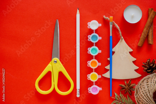 New year DIY background, creativity with children, make a gift with your own hands. Scissors, twine, pine cone, paint brush, wooden spruce on a red background. Home decoration for the holiday