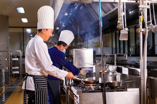 Asian male chef cooking food with his colleuge in the hotel kitchen