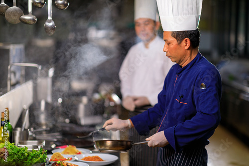 Male chef cooking in the restuaranr kitchen with his team.