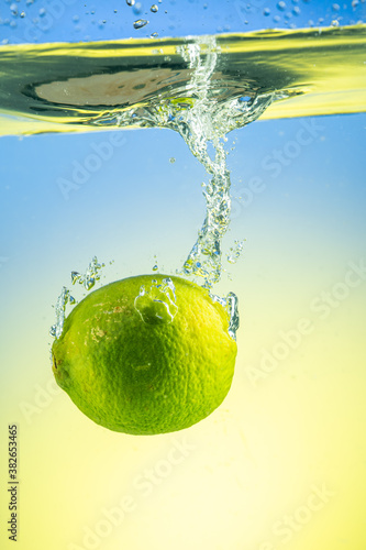 Whole green lime drops under water with splashes on gradient background