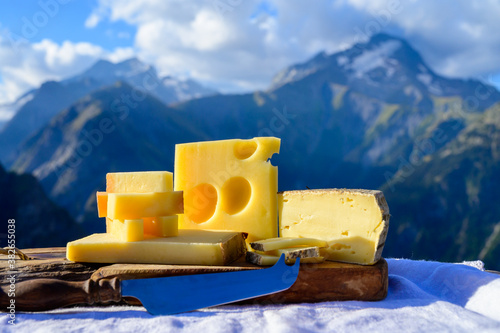 Cheese collection, French beaufort, abondance, emmental, tomme de savoie cheeses served outdoor in Savoy region, with Alpine mountains peaks on background photo