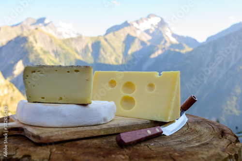 Cheese collection, French emmental, tomme and reblochon de savoie cheeses served outdoor in Savoy region, with Alpine mountains peaks on background photo