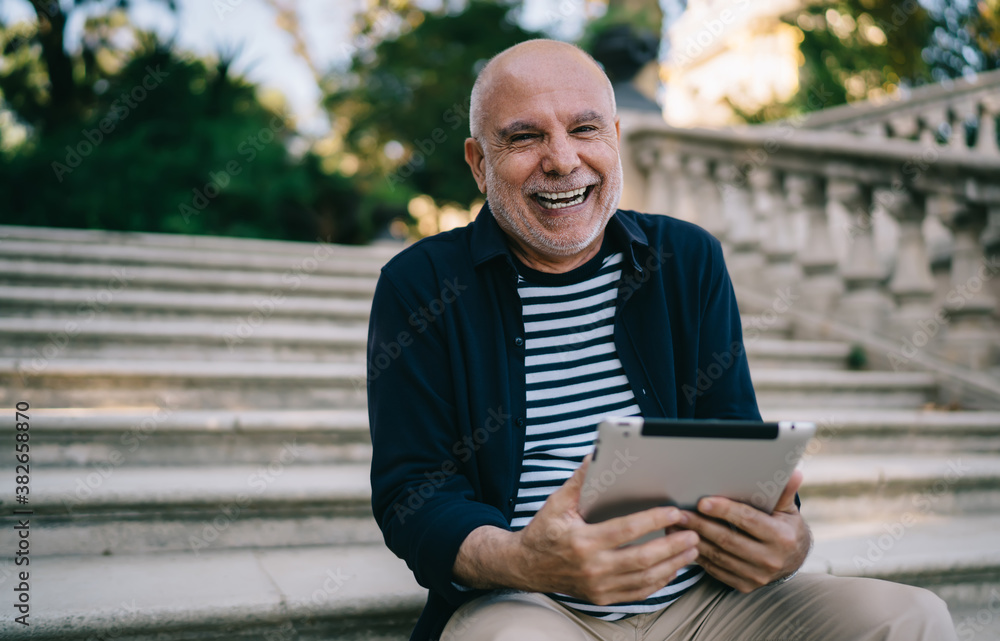 Laughing aged man using tablet on stairs in park Laughing aged man using tablet on stairs in park