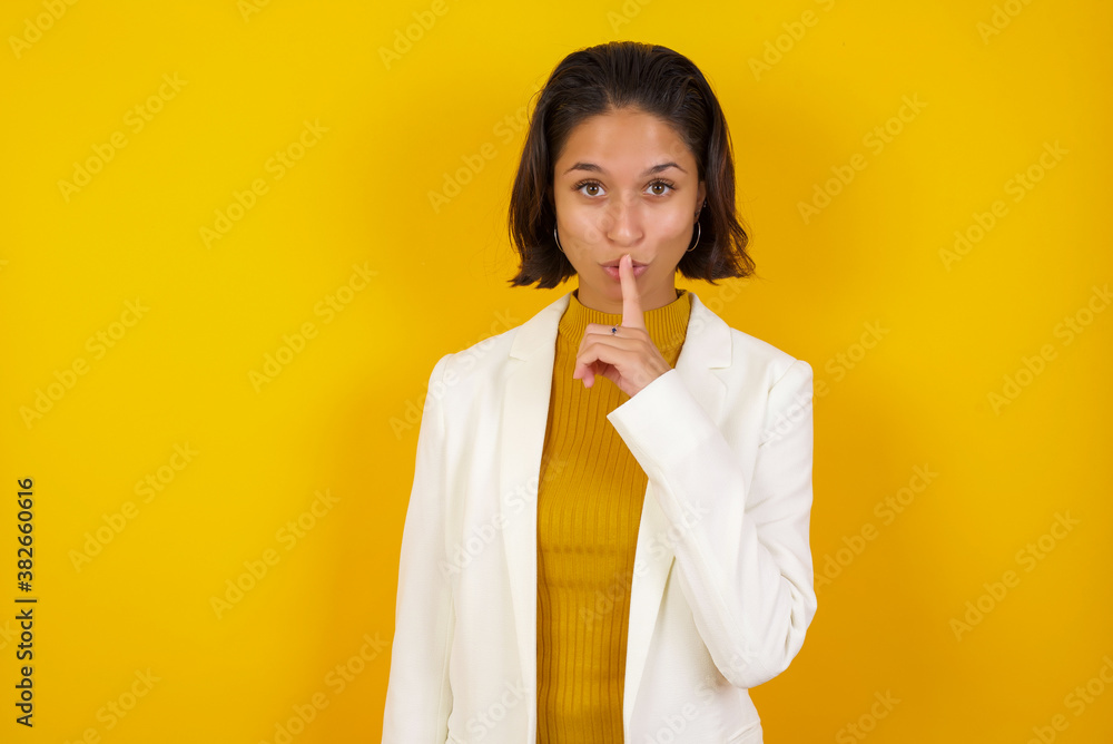 Dont tell my secret or not speak too loud, please! Emotional surprised student makes hush gesture, asks be quiet, has scared expression as afraids of revealing secret, poses against gray studio wall. Dont tell my secret or not speak too loud, please! Emotional surprised student makes hush gesture, asks be quiet, has scared expression as afraids of revealing secret, poses against gray studio wall.