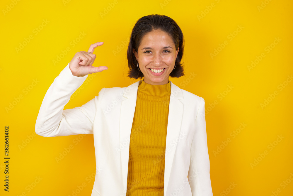 Blonde European woman over isolated background gesturing with hand showing small size, measure symbol. Smiling looking at the camera. Measuring concept.