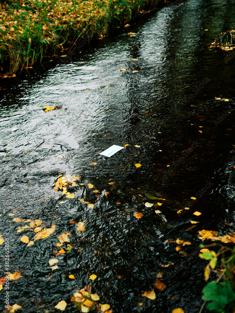 A face mask floats down a stream or river. Symbolic for the covis-19 times and the environment. Pollution in the nature. A face mask floats down a stream or river. Symbolic for the covis-19 times and the environment. Pollution in the nature.
