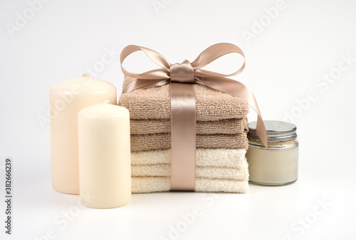 Spa set of beige and white towels tied with a satin ribbon, candles and cream, on a white background. Gift set, side view horizontal orientation. Concept of Spa treatments. photo