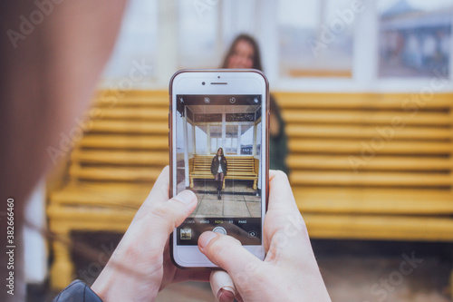 amiga tomando una foto con el móvil de una mujer junto a un banco amarillo en tarde de invierno photo