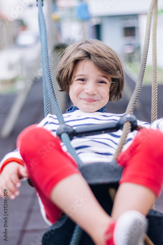 Vertical photo of a little girl with short hair on a swing in a playground with the background out of focus
