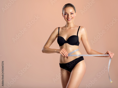 Young smiling woman with tape and a beautiful, healthy body. Sexy woman measuring her perfect body.