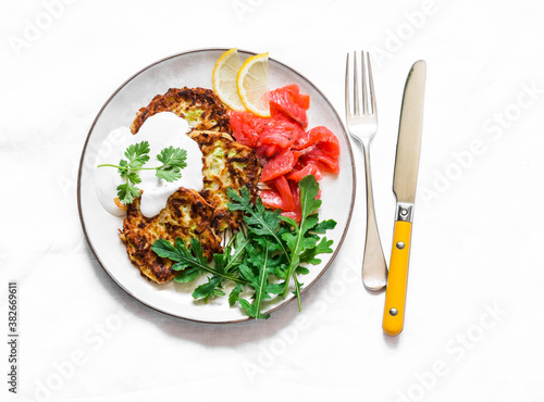 Zucchini and latkes with smoked salmon, sour cream and arugula. Delicious breakfast, brunch, tapas, appetizer on a light background, top view