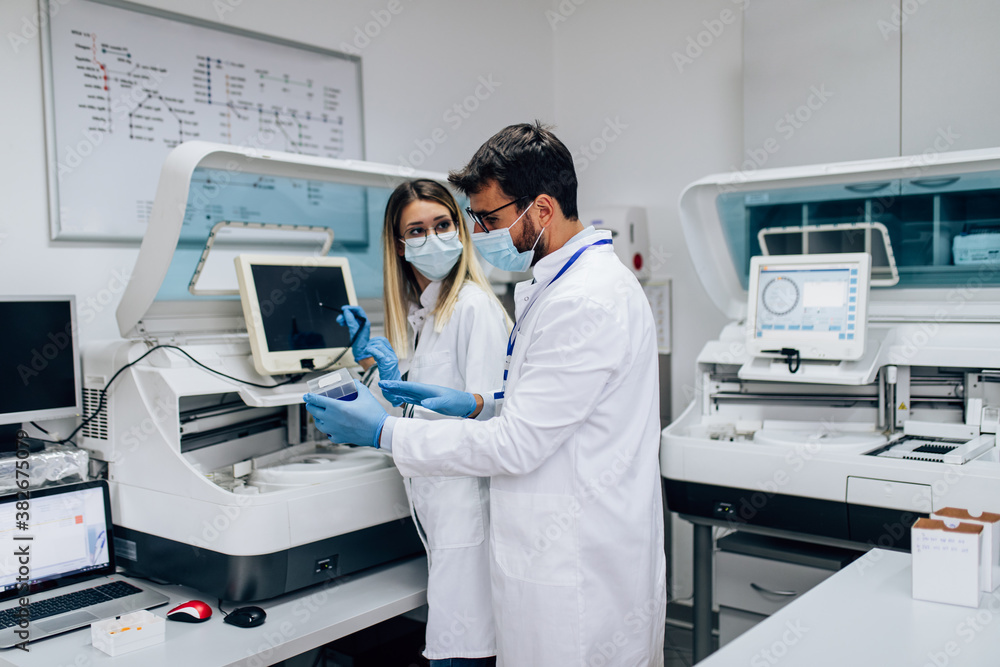 Two scientists or technicians with face protective masks work in laboratory on human blood samples. Two scientists or technicians with face protective masks work in laboratory on human blood samples.