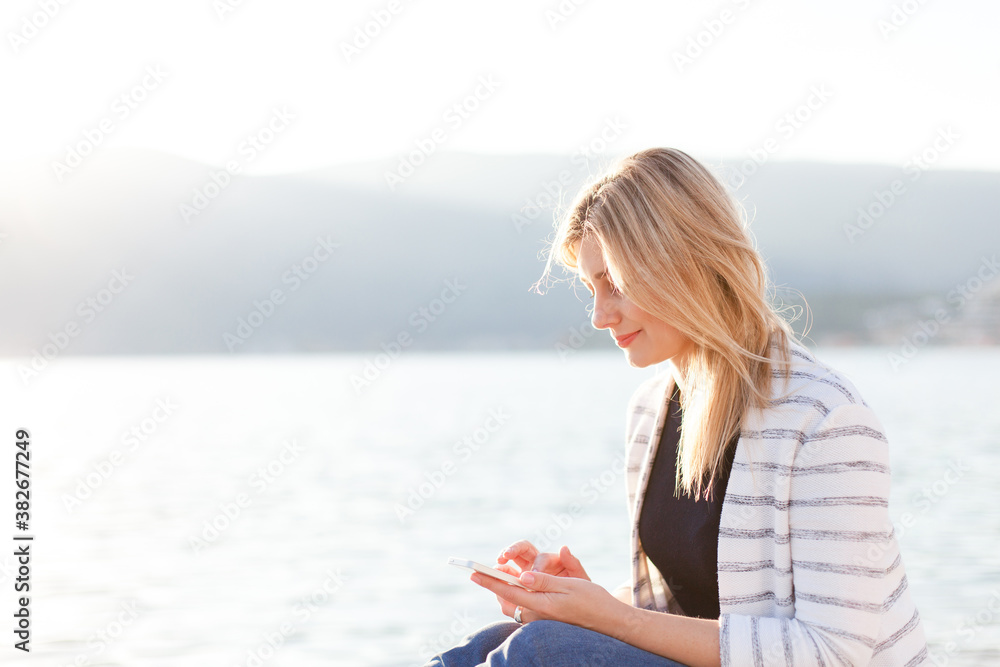 Young woman using mobile phone on sea beach at sunset. People virtual connection, communication. Lifestyle moment.