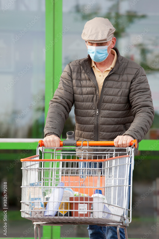 Mature man with face mask leaving a supermarket with a shopping cart