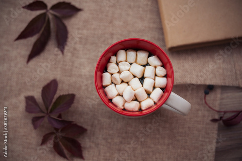 Autumn photo in warm colors glass of coffee and marshmallows on the table with red leaves , top view