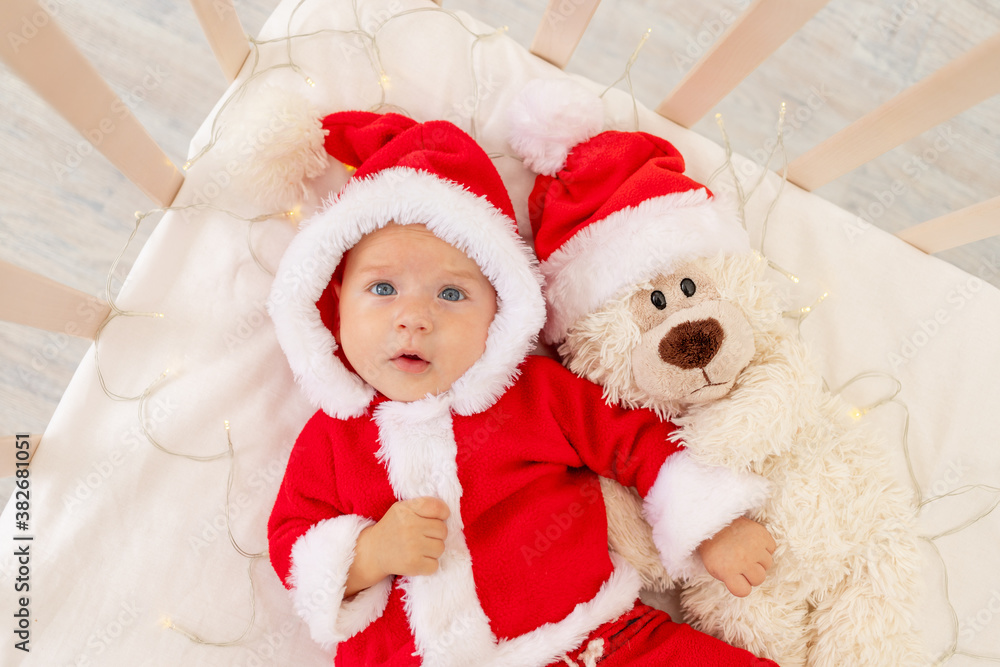 Christmas photo of a baby in a Santa costume lying in a crib at home with a toy in a Santa Claus hat, top view, happy new year Christmas photo of a baby in a Santa costume lying in a crib at home with a toy in a Santa Claus hat, top view, happy new year