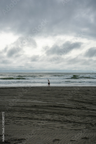 A Lonely Man Walking Across the Beach With A Dramatic Stormy Sky Behind Him