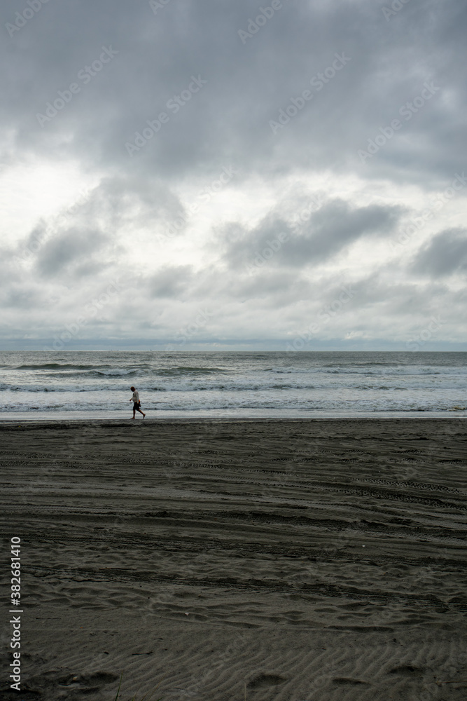 A Lonely Man Walking Across the Beach With A Dramatic Stormy Sky Behind Him