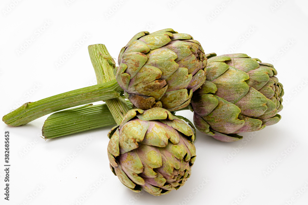 Three organic artichokes with a piece of stem on a white surface. Three organic artichokes with a piece of stem on a white surface.