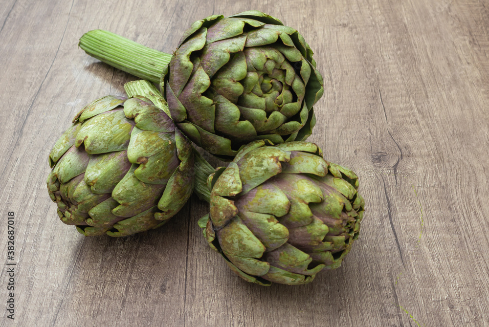 Fototapeta premium Three fresh organic purple artichokes with stem on a rustic wooden surface and dark background