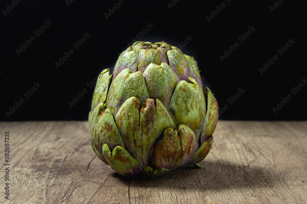 Obraz premium close-up of a fresh, organic artichoke just grown on a rustic wood surface and a black background.