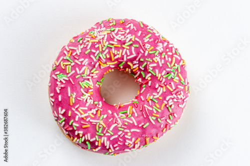 A pink doughnut decorated with multicolored splashes lies on a white table. The view from the top