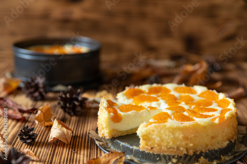 Cheesecake oder Käsekuchen mit fruchtigen orangen Mandarinen auf einem Tisch aus Holz im Herbst mit Laubblättern