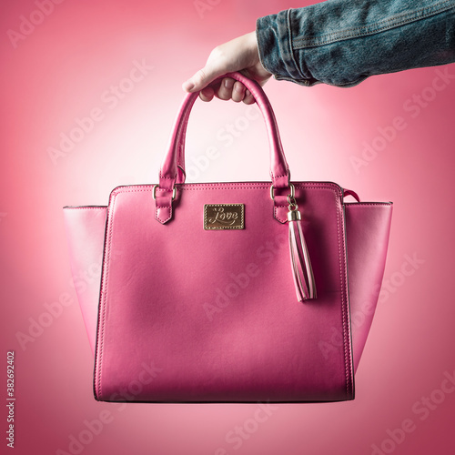 hand holding a pink handbag on a monochromatic pink background 