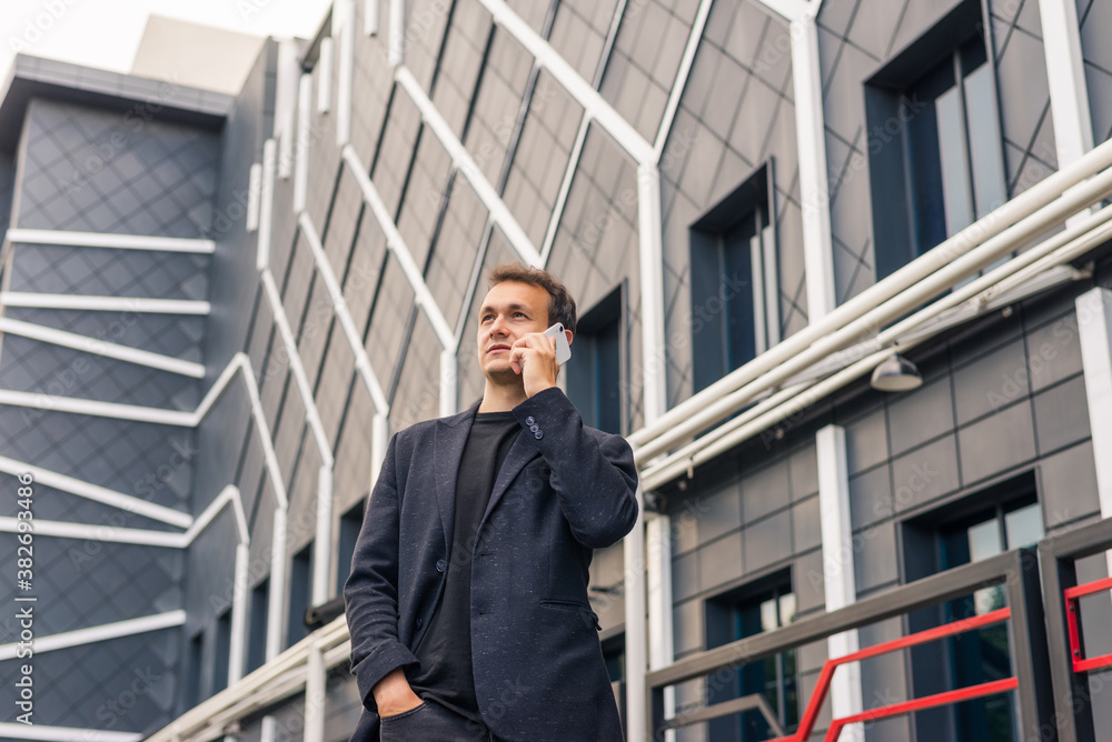 Portrait of handsome young businessman talking on mobile phone near business center