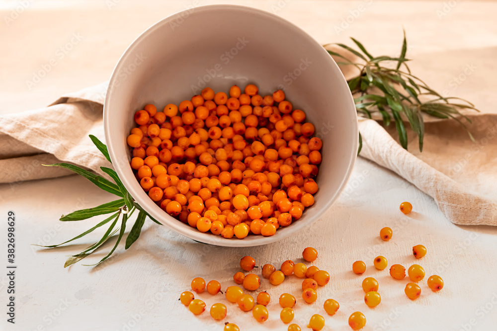 Freshly picked sea buckthorn berries in a grey bowl on light grey concrete background Freshly picked sea buckthorn berries in a grey bowl on light grey concrete background