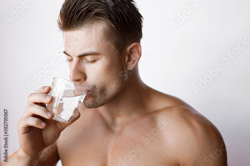 Muscular sexy model sports young man on white background. Portrait of beautiful smiling healthy guy holding a glass of water.