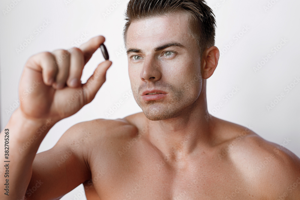 Muscular sexy model sports young man on white background. Portrait of beautiful smiling healthy guy holding a pill in his hand. Muscular sexy model sports young man on white background. Portrait of beautiful smiling healthy guy holding a pill in his hand.