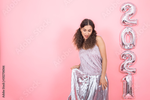 Young woman on a pink background with silver balls in the form of the numbers 2021 photo