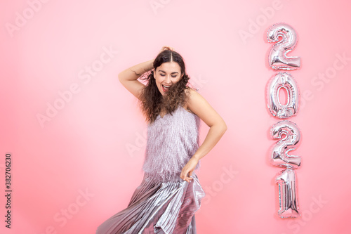 Young woman on a pink background with silver ballons in the form of the numbers 2021 photo