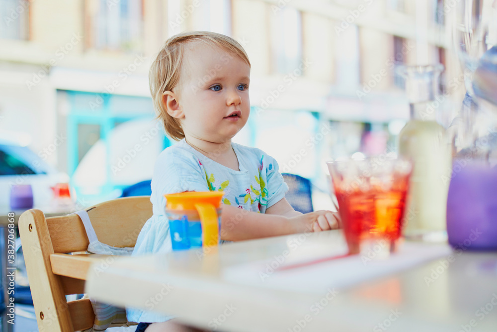 Adorable toddler girl sitting in high chair in cafe or restaurant Adorable toddler girl sitting in high chair in cafe or restaurant
