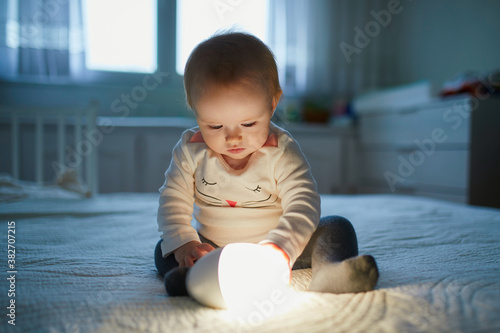 Tableau sur toile Adorable baby girl playing with bedside lamp in nursery