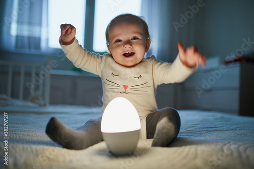 Fotografie Adorable baby girl playing with bedside lamp in nursery