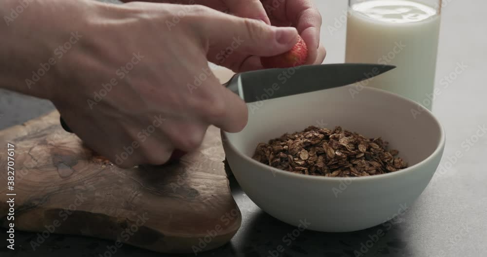 Slow motion closeup man hands slicing fresh strawberries into chocolate granola Slow motion closeup man hands slicing fresh strawberries into chocolate granola
