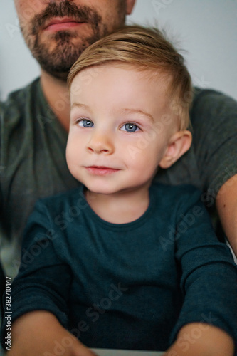 Youngster sitting in father's lap and looking at camera with his beautiful big blue eyes.