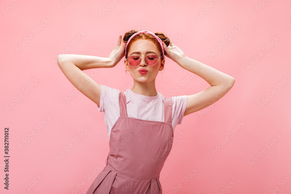Lovely girl with buns dressed in pink overalls and white T-shirt posing with closed eyes on pink background Lovely girl with buns dressed in pink overalls and white T-shirt posing with closed eyes on pink background