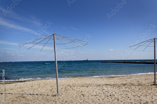 Lonely sandy empty autumn beach with metal umbrellas silhouette and blue sea water horizon at the end of summer season  