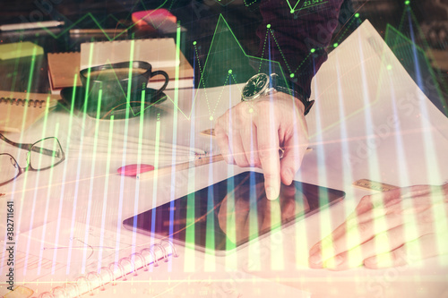Double exposure of man's hands holding and using a digital device and forex graph drawing. Financial market concept.