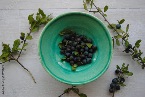 Blackthorn or Prunus Spinosa placed in a ceramic bowl on the white wooden background. Top view.