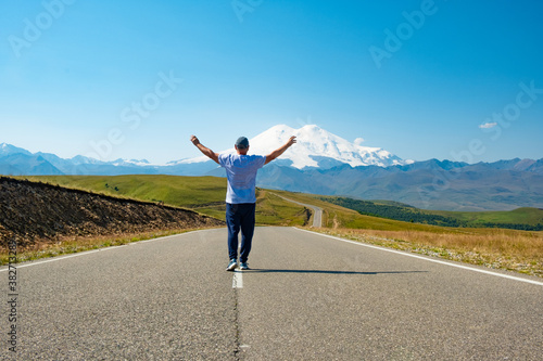 A man walks along the highway against the backdrop of mountains. Freedom and travel concept. Elbrus, Caucasus. © margo1778