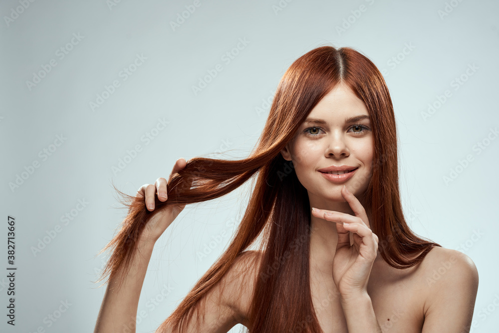 Obraz premium pretty redhead woman holding her hair with hands grooming naked shoulders light background