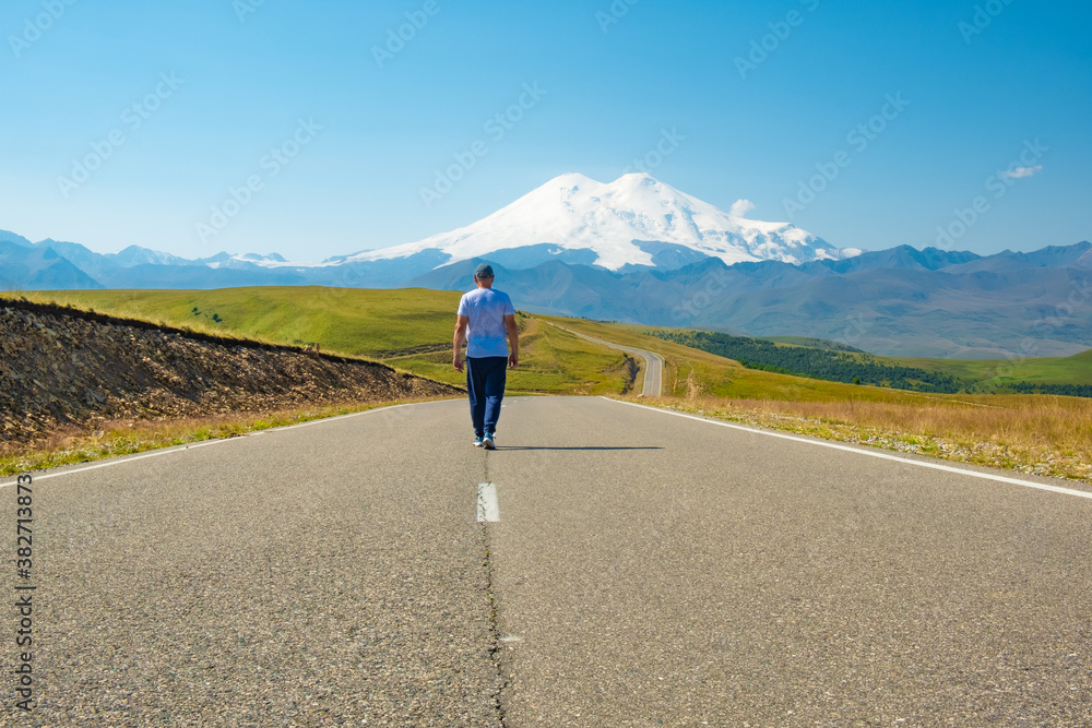 A man walks along the highway, against the background of mount Elbrus. Mountain landscape. Freedom and travel concept