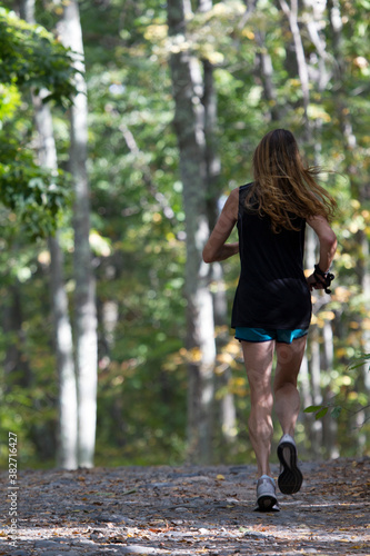Female runner running at autumn park trail in forest.