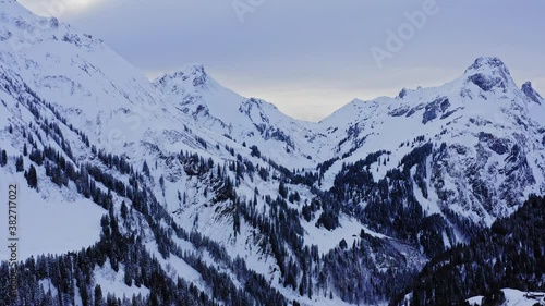 snow covered mountains in the german alps. Trees in the valley and cloudy sky view in the winter. 